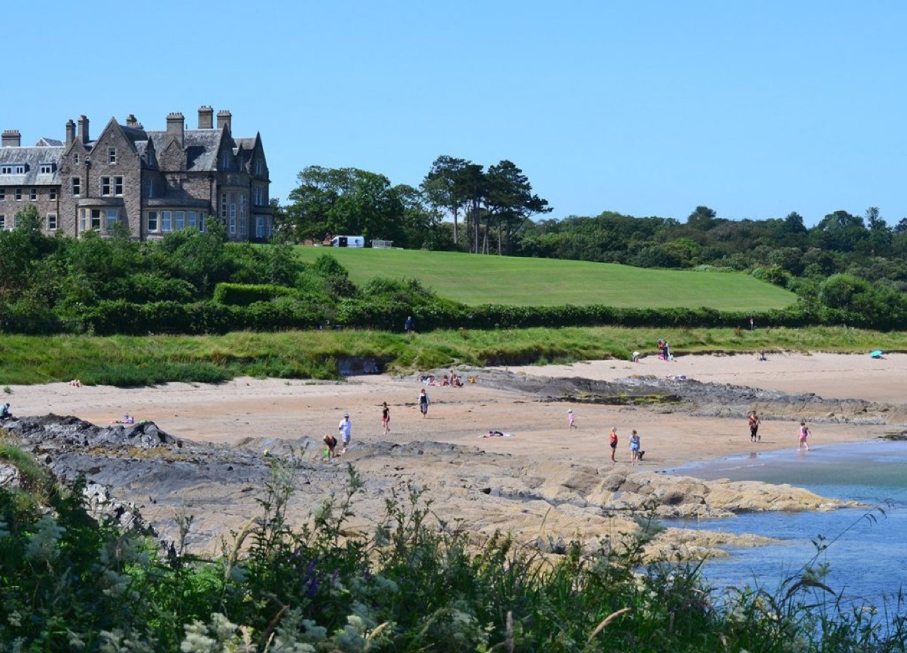 A wide sandy beach at Crawfordsburn framed by trees and green slopes above the shore