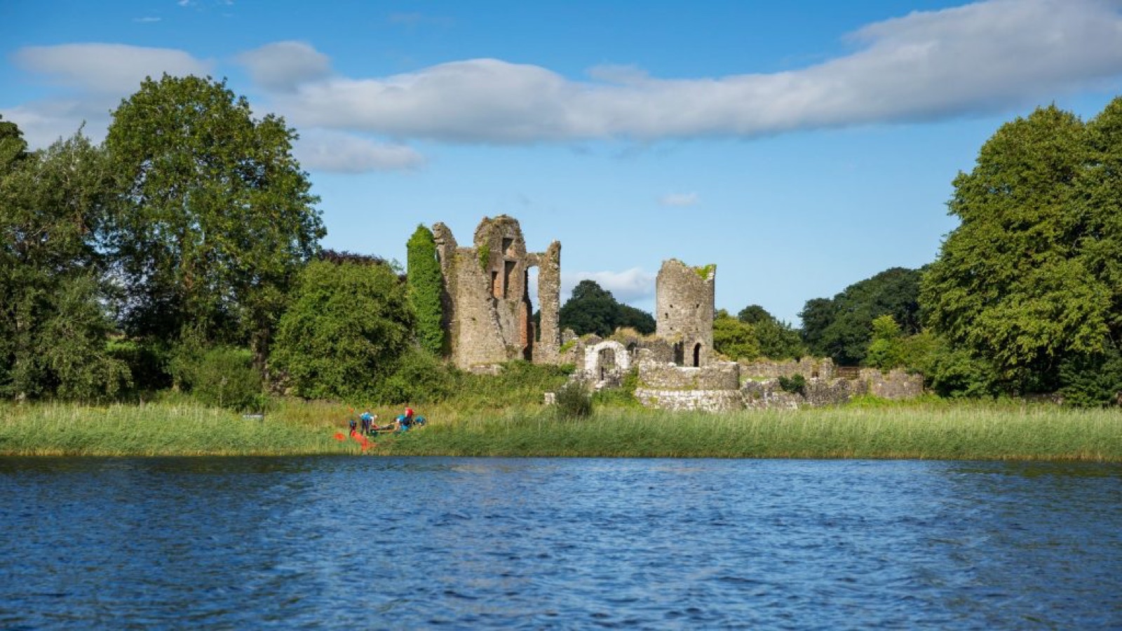 The grey Old Castle ruins at Crom Estate rising above reeds on the far shore of Upper Lough Erne under a blue sky