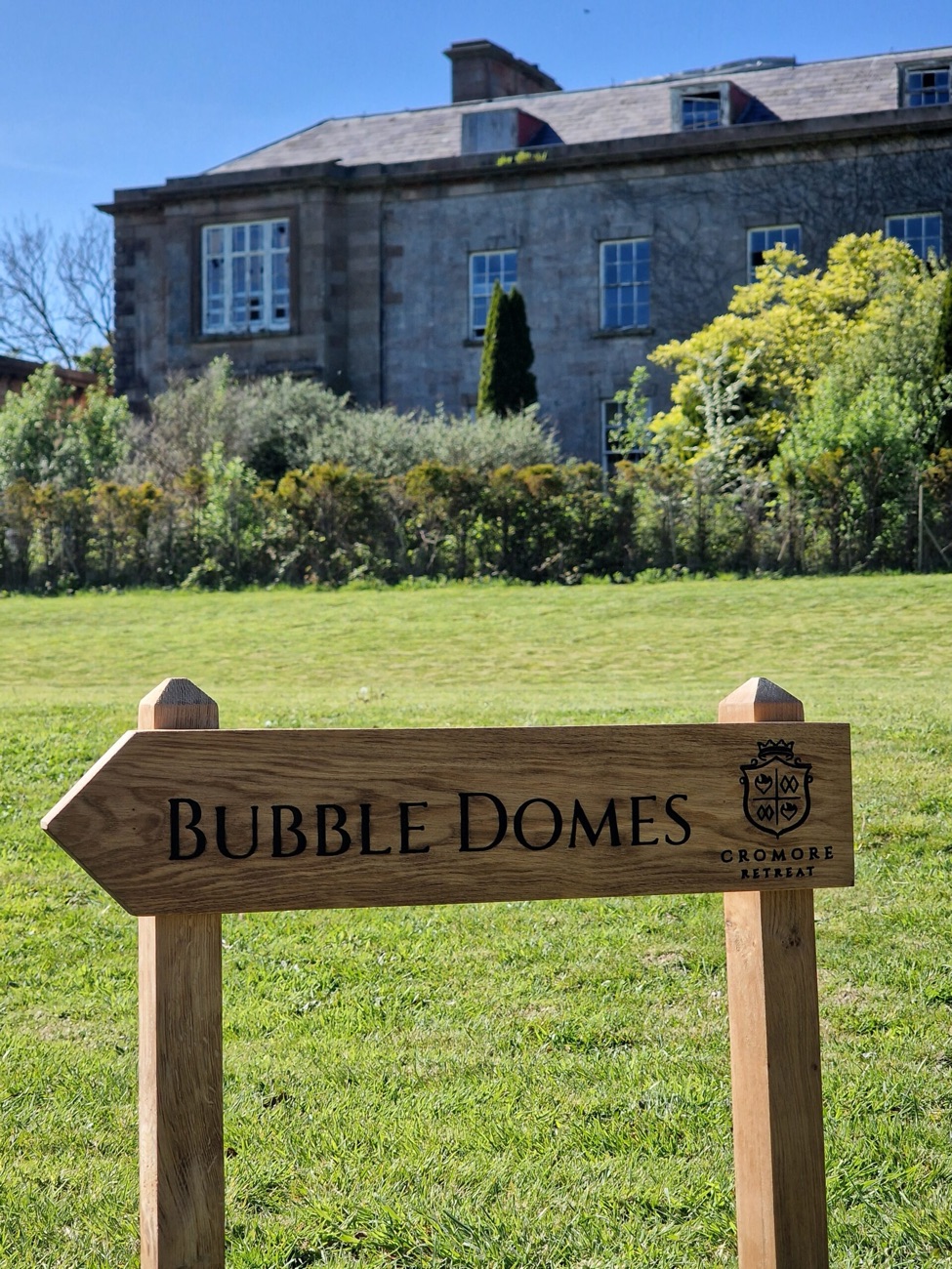 Cromore House behind a lawn, with a wooden estate sign in the foreground for the retreat now on the grounds