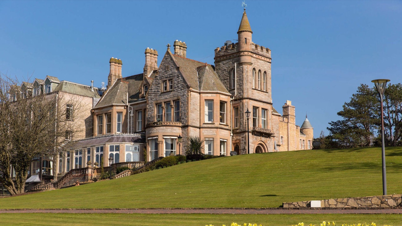 The Victorian estate house in warm sandstone, set above sloping green lawns.