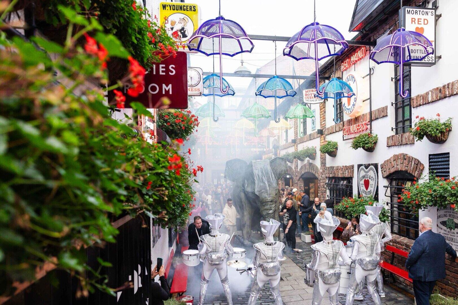 Performers in glowing silver LED costumes drumming in the umbrella-lined Commercial Court in Belfast's Cathedral Quarter