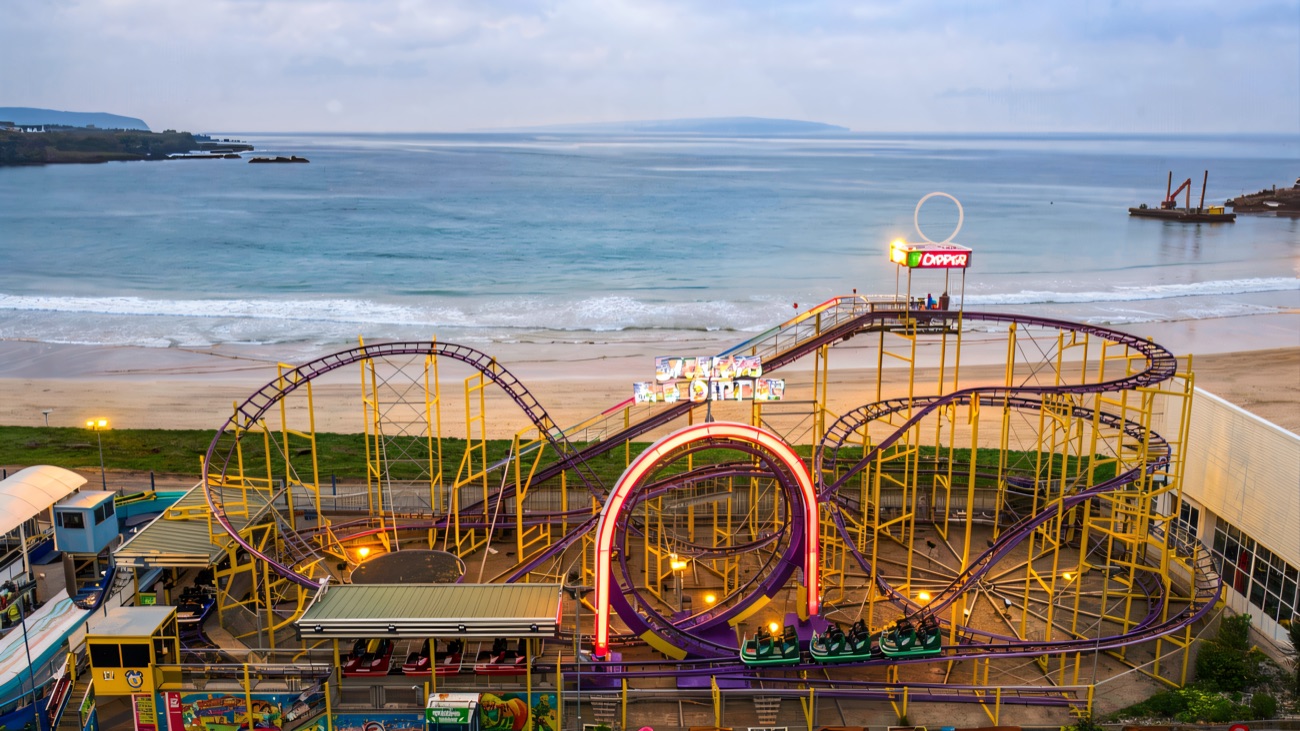 Aerial view of the purple and yellow Big Dipper roller coaster at Curry's Fun Park with the beach and sea right behind it