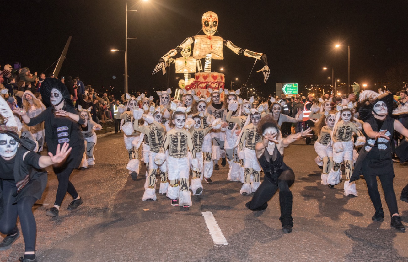 The Derry Halloween Carnival Parade at night with a towering skeleton puppet and performers in skeleton costumes