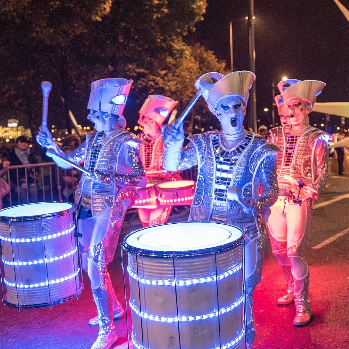 Performers in glowing silver LED costumes drumming in the street at Derry Halloween