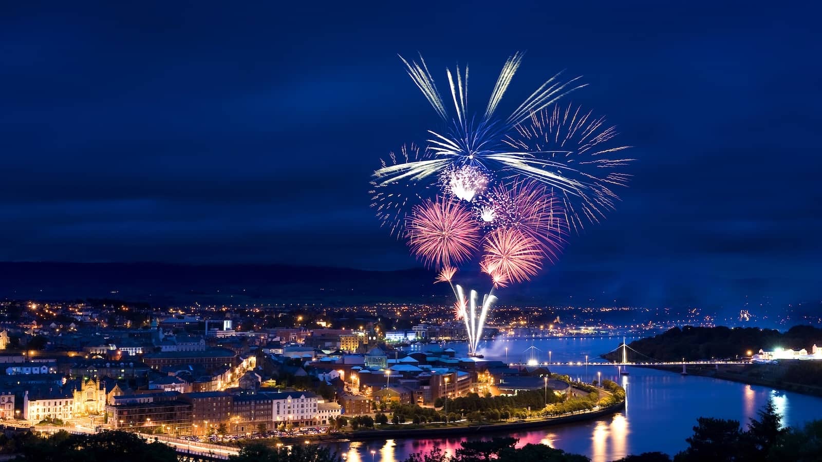 Fireworks bursting over the River Foyle above the lights of Derry at night during Halloween