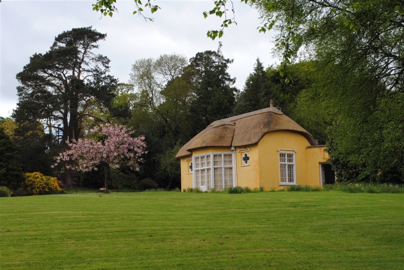 Derrymore House across the sweeping parkland lawn, with a pink cherry blossom tree in flower and mature woodland behind