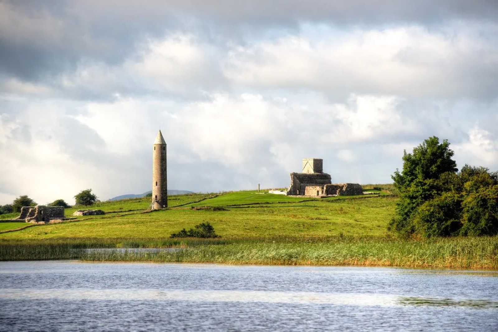 Devenish Island seen from the water — the tall round tower and grey church ruins on a green island under a moody sky, Lough Erne in front