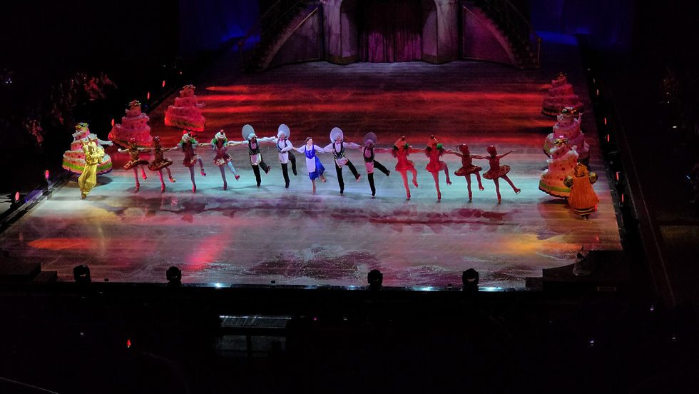 Disney On Ice skaters in bright costumes performing under stage lights at an arena show
