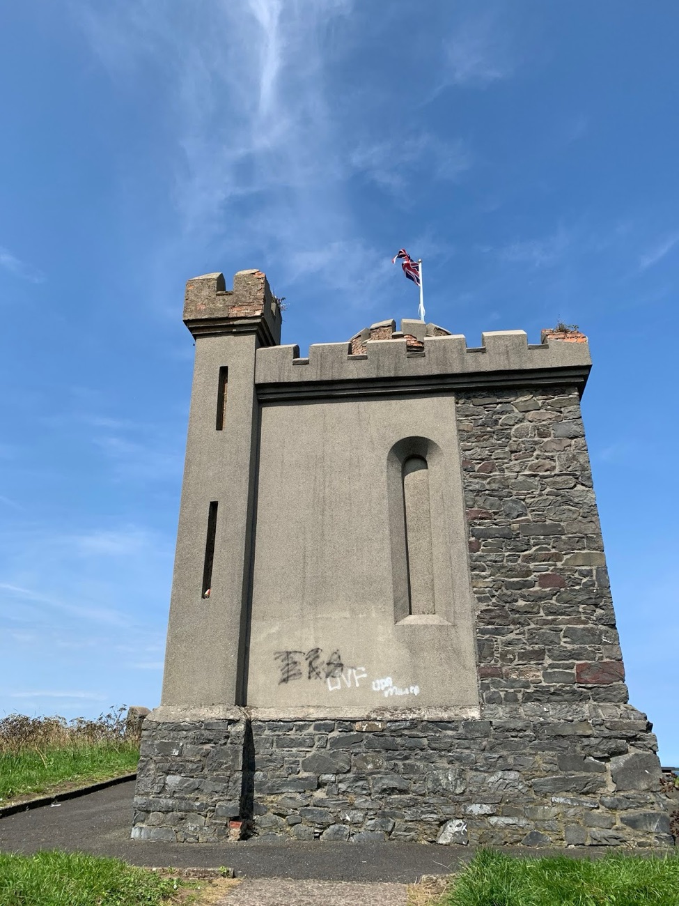 The restored castellated gunpowder store on top of the motte at Donaghadee, flag flying against a blue sky