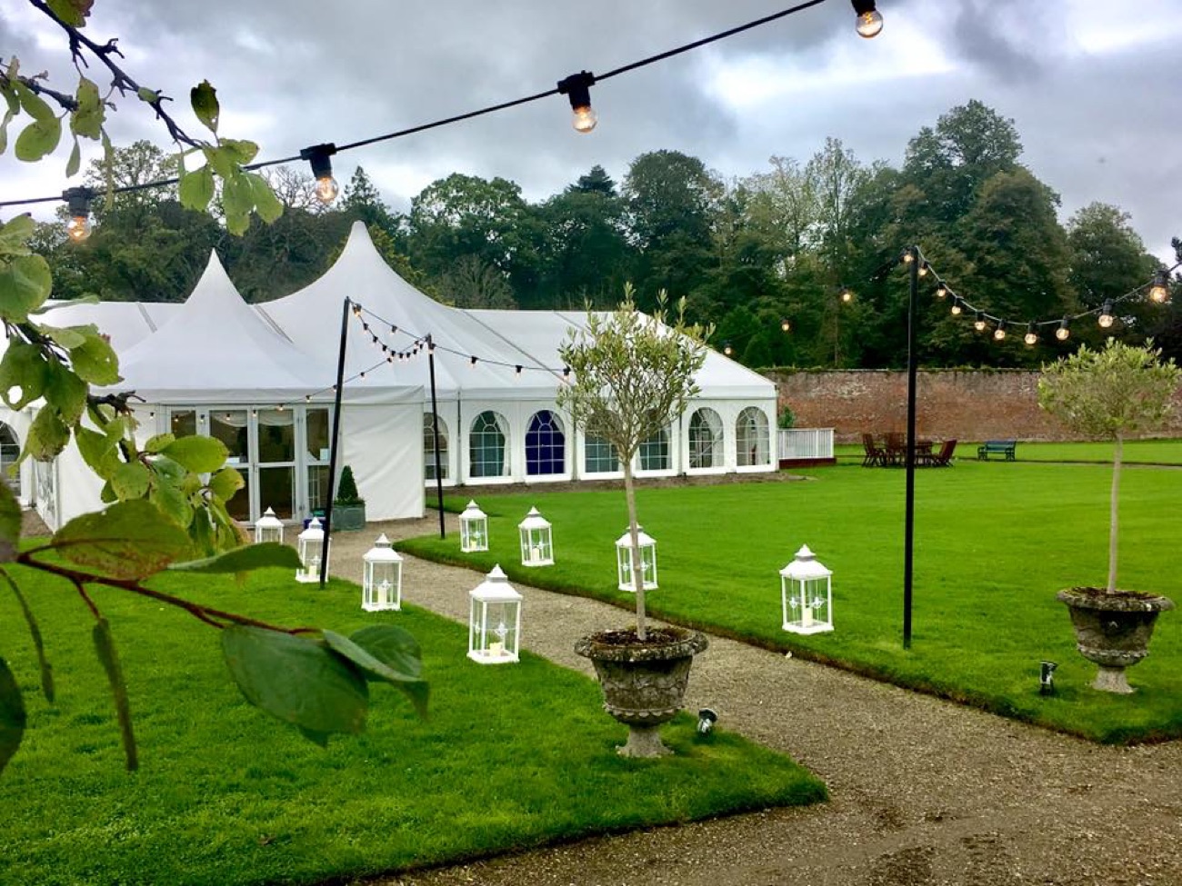 A white events marquee in the walled garden strung with festoon lights and lanterns