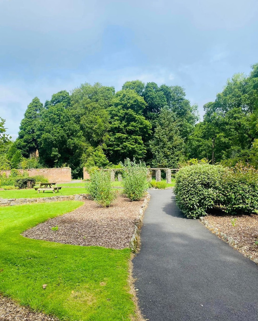 The walled garden at Drum Manor with a gravel path, planted beds, a picnic table and old brick walls with arched gateways
