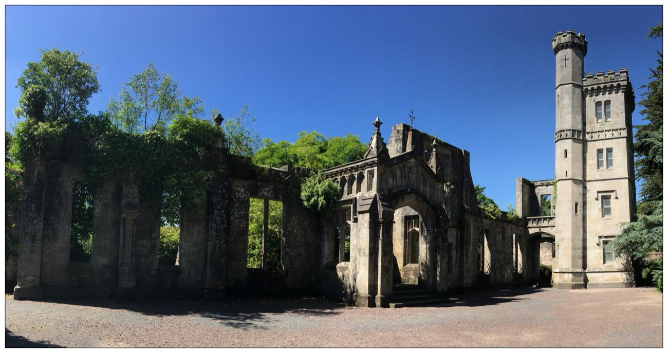 The full ruins of Drum Manor house against a blue sky, the roofless stone walls and the surviving battlemented tower
