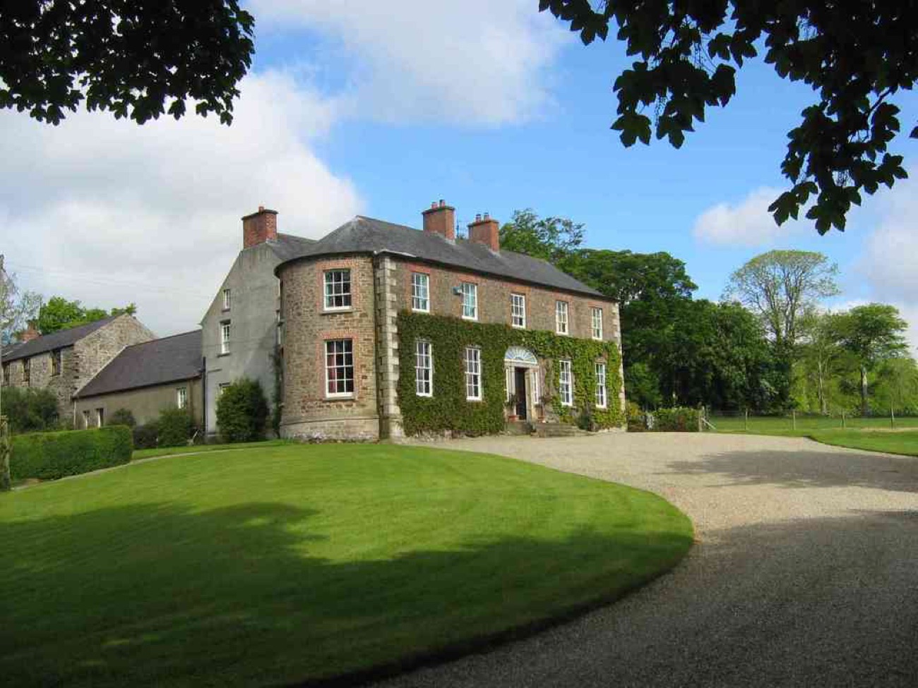 The ivy-clad Georgian facade of Drumcovitt House with its bow tower and brick chimneys, a broad green lawn and gravel sweep in front