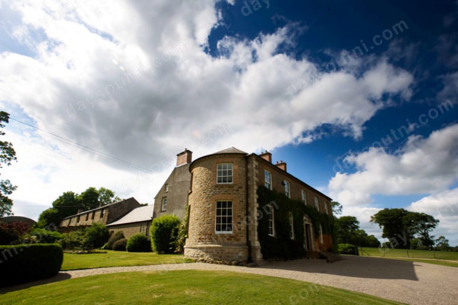 The stone Georgian front of Drumcovitt House with its rounded bow-fronted tower, sash windows and ivy, above a curving lawn and gravel drive