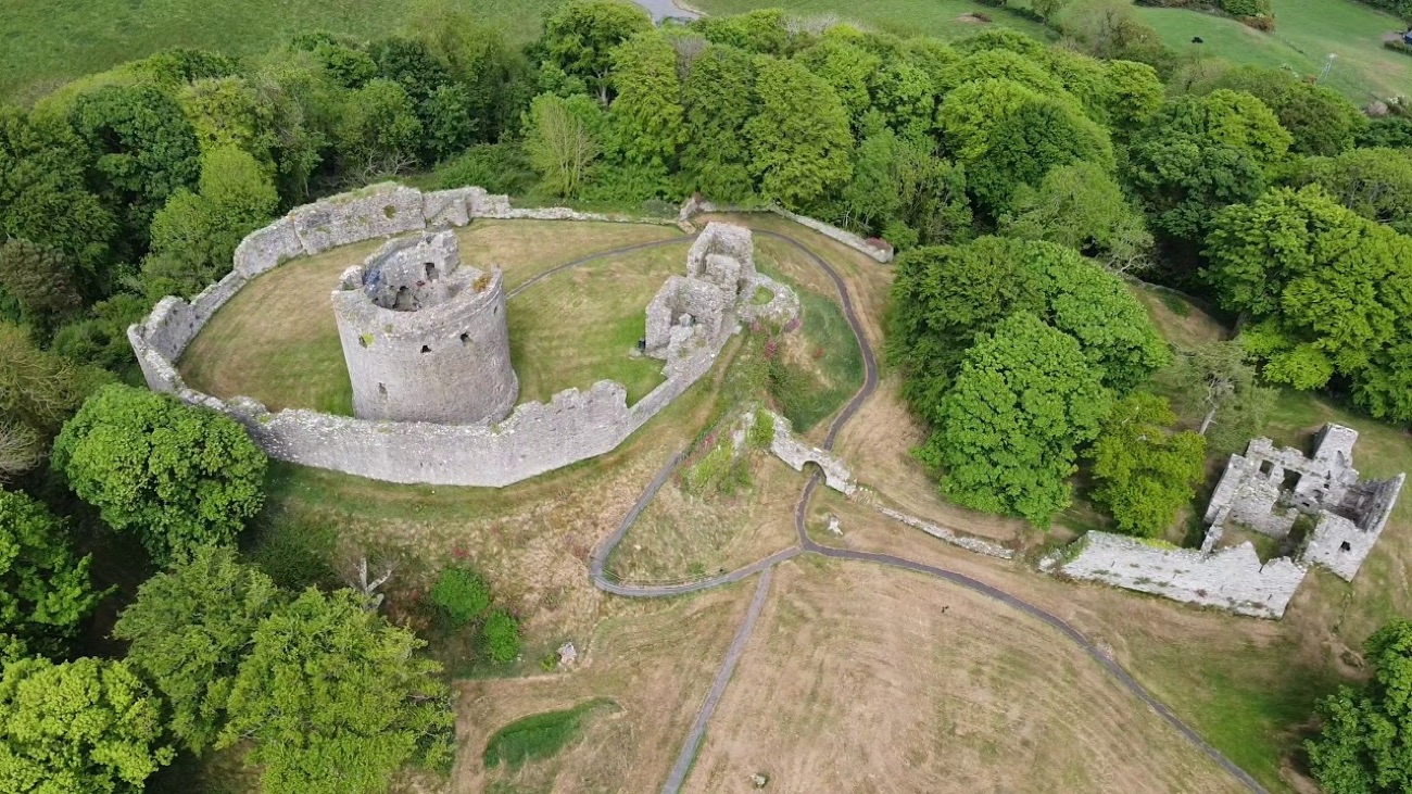 Aerial view of the whole Dundrum Castle ruin on its hilltop — round keep, curtain walls and grassy bailey
