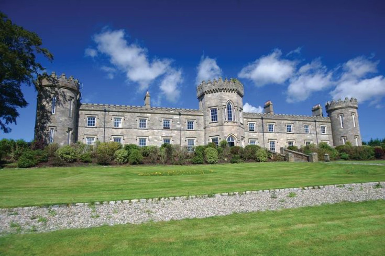 The full castellated front of Dungiven Castle with three round turrets under a bright blue sky