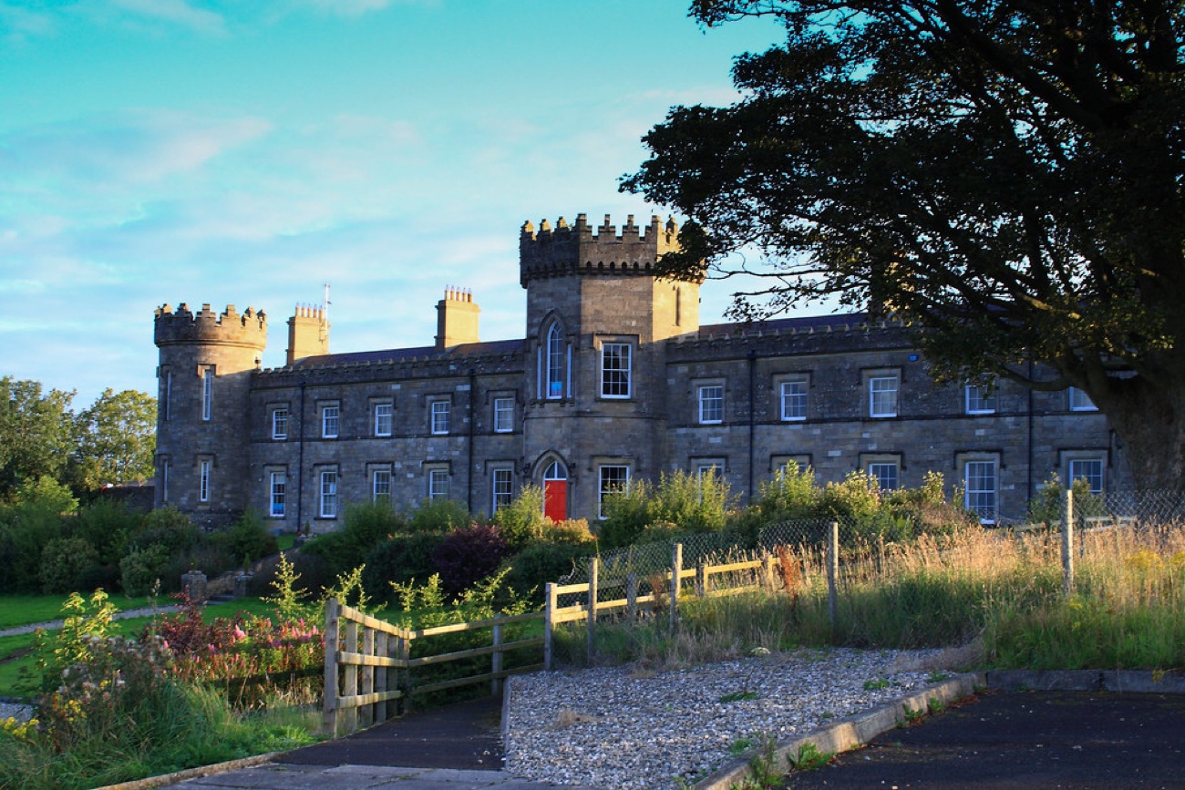A warm evening view of Dungiven Castle's tower and red door framed by a large tree
