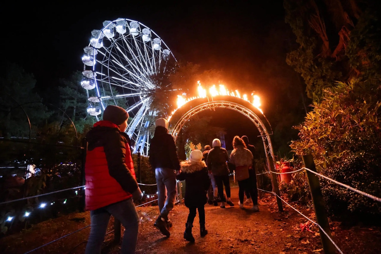 Families walking the illuminated trail beneath a flaming arch at the Enchanted Winter Garden in Antrim