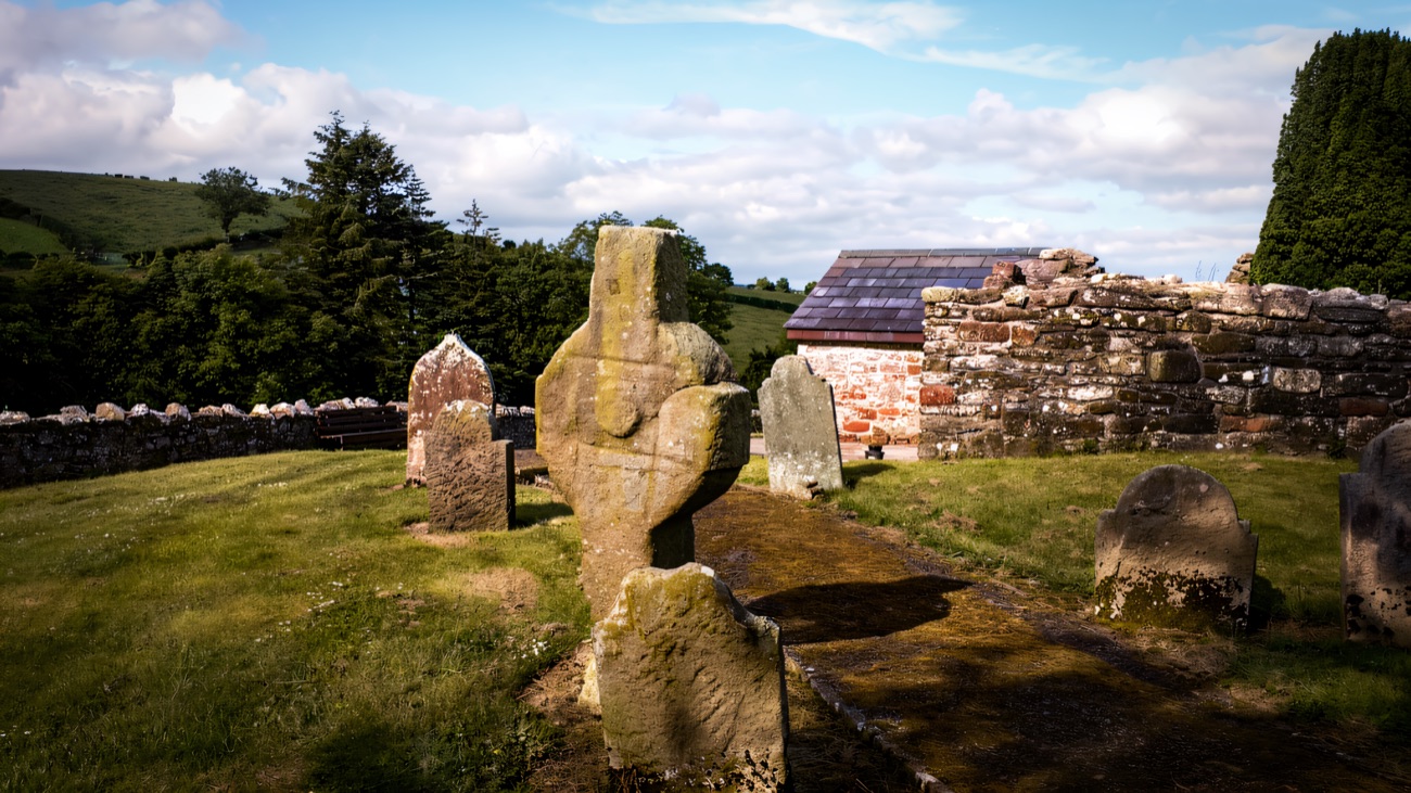 The ancient cross standing in the graveyard beside the church ruin, hills rolling beyond