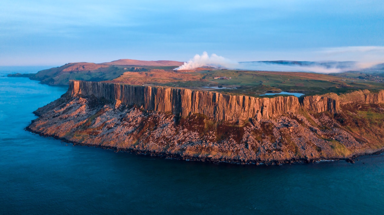 Golden-hour aerial view of the whole Fair Head headland, its cliff face and the plateau lough behind