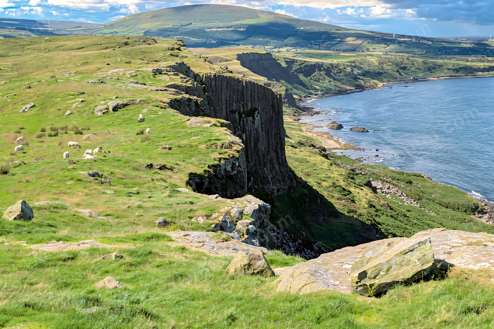 The dolerite columns of Fair Head rising above the green headland and the blue bay near Ballycastle