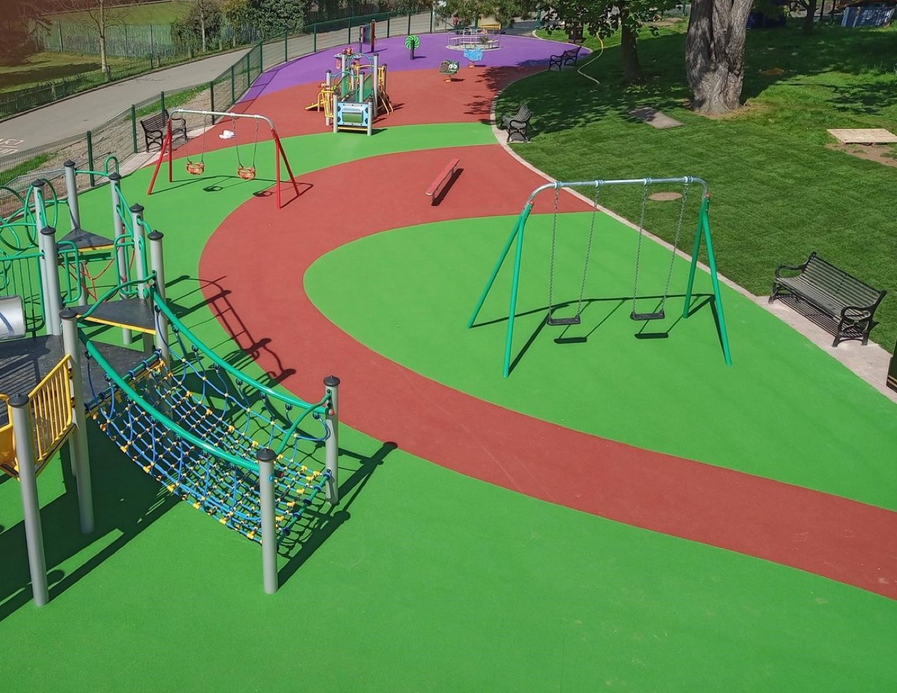 The refurbished play park at Falls Park with swings, a net climber and coloured safety surfacing