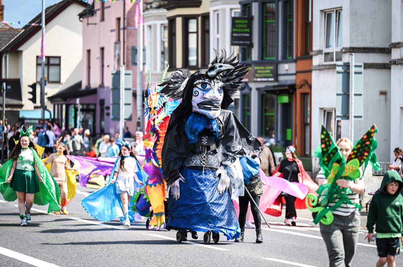 A giant carnival puppet and costumed performers with flowing fabric in the Féile carnival parade in West Belfast