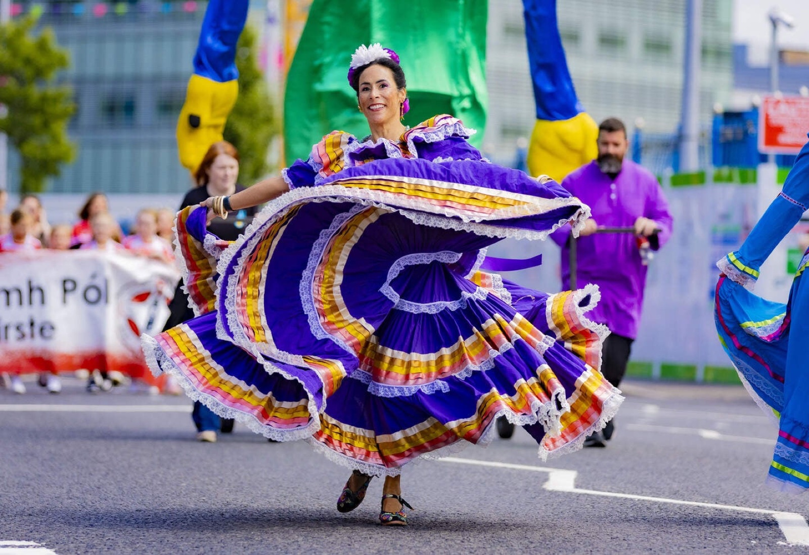 A dancer in a vivid purple and gold Mexican folk dress spinning in the Féile an Phobail carnival parade