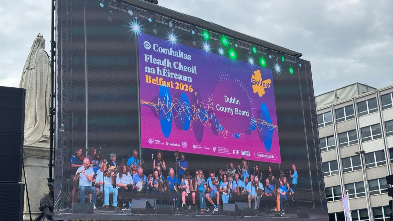 A giant screen reading Fleadh Cheoil na hÉireann Belfast 2026 above a traditional Irish music orchestra