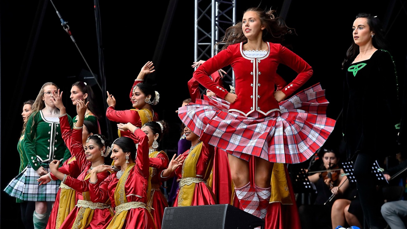 Irish and South Asian dancers in colourful costumes performing together on stage at the Fleadh Cheoil