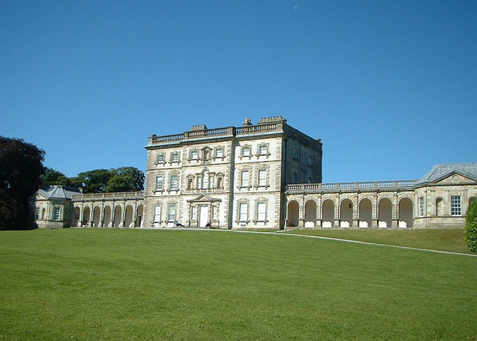 The grey Georgian house at Florence Court with its curved colonnade wings and a wide green lawn under a big sky