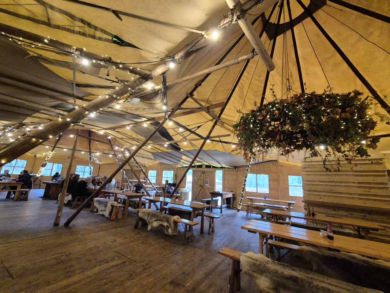 The wide tipi interior at Fodder with long wooden benches, string lights and a hanging wreath
