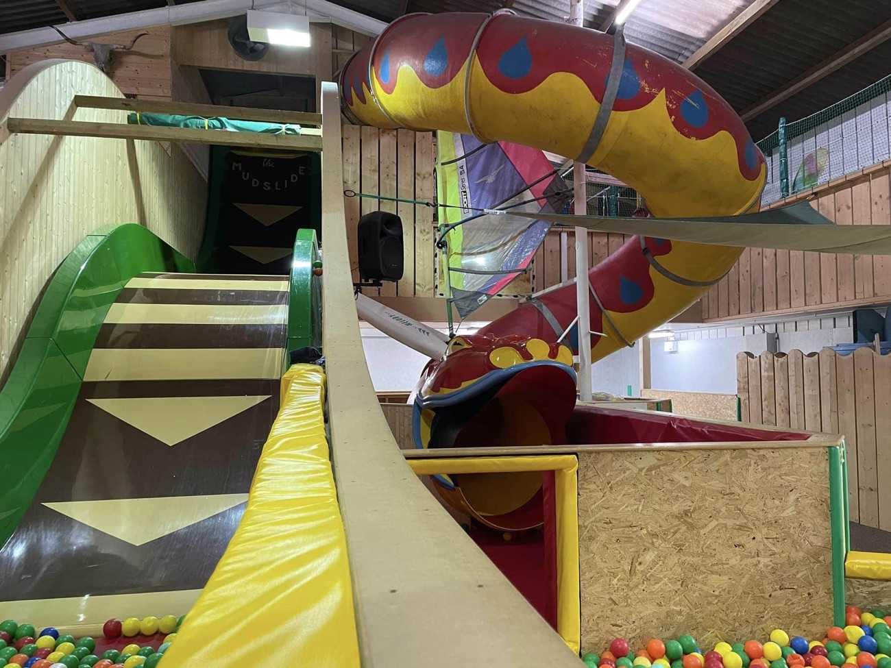 A green wave slide beside a red-and-yellow spiral dragon tube slide inside the indoor play barn