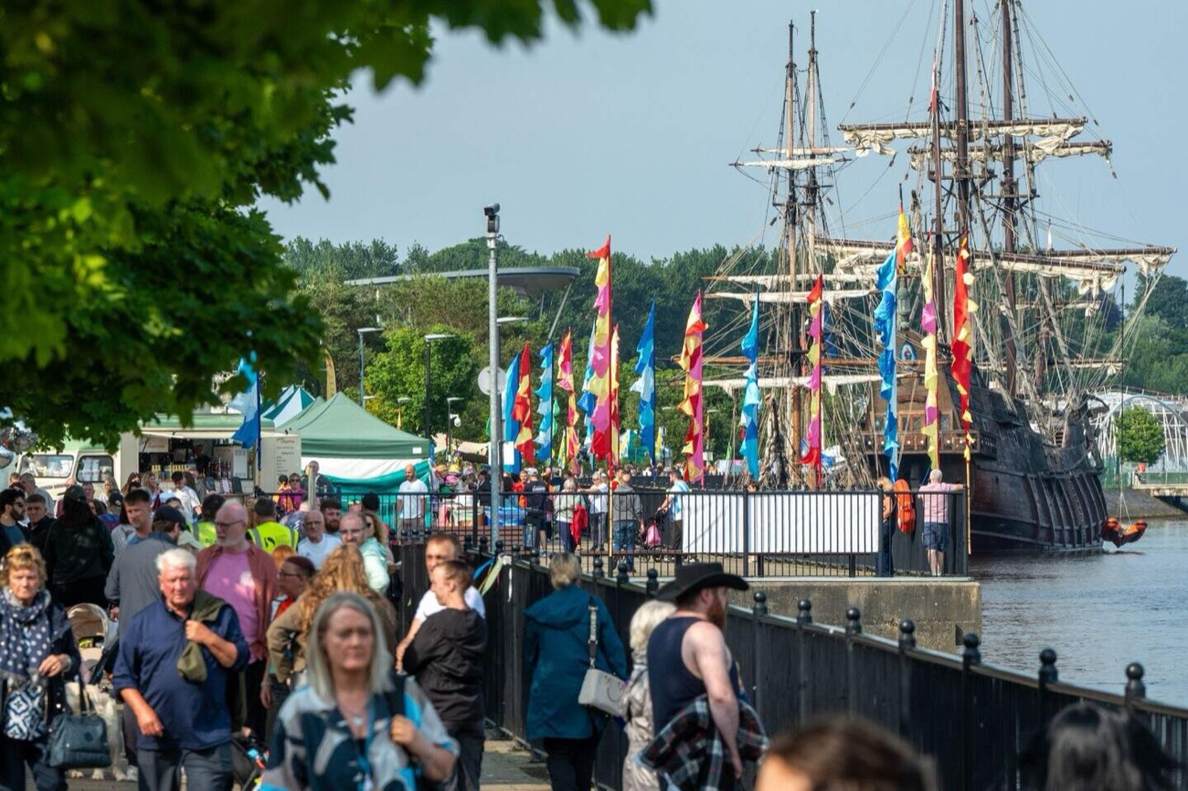 Crowds and colourful flag banners along the festival quay with a tall galleon moored beside them