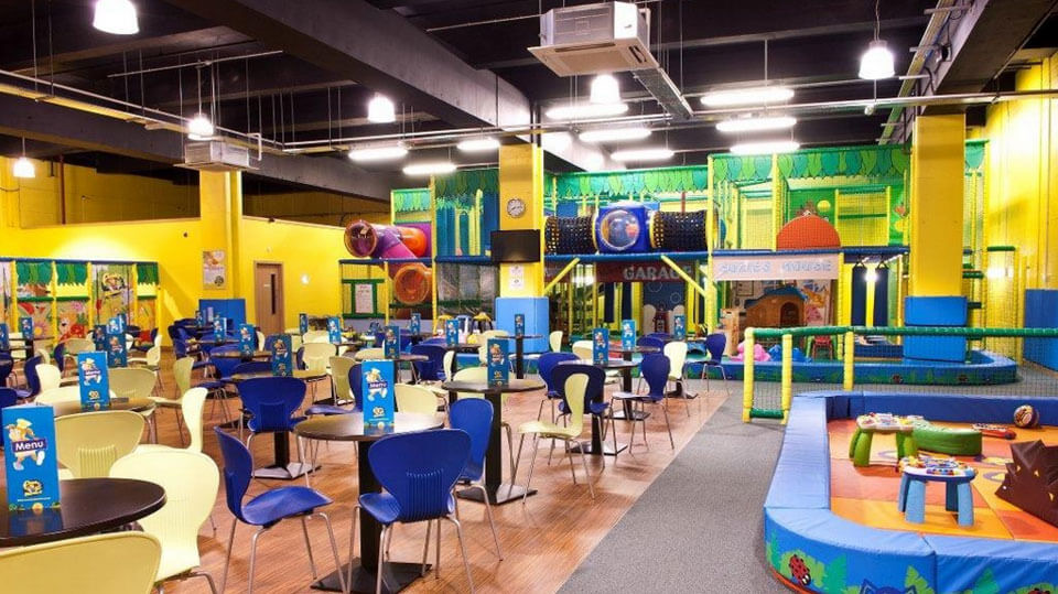 The big jungle-themed soft play frame at Funky Monkeys Cityside, Belfast, with café tables in the foreground and a toddler soft-play area to the side