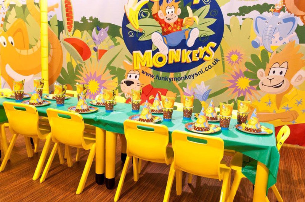 A birthday party room at Funky Monkeys set with a green table, yellow chairs and a colourful jungle mural