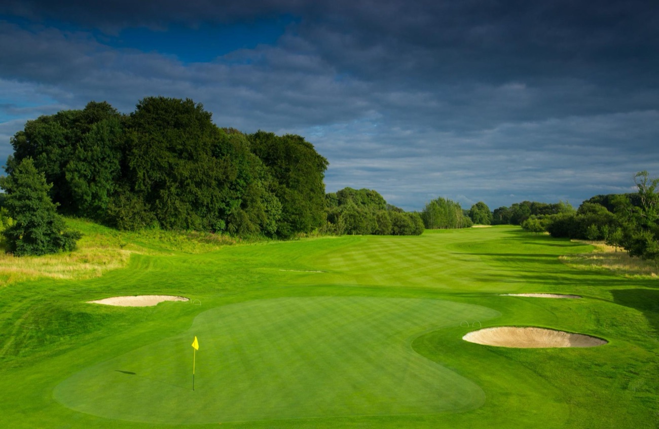 A manicured green with bunkers and flag on the Galgorm Castle golf course under a dramatic sky