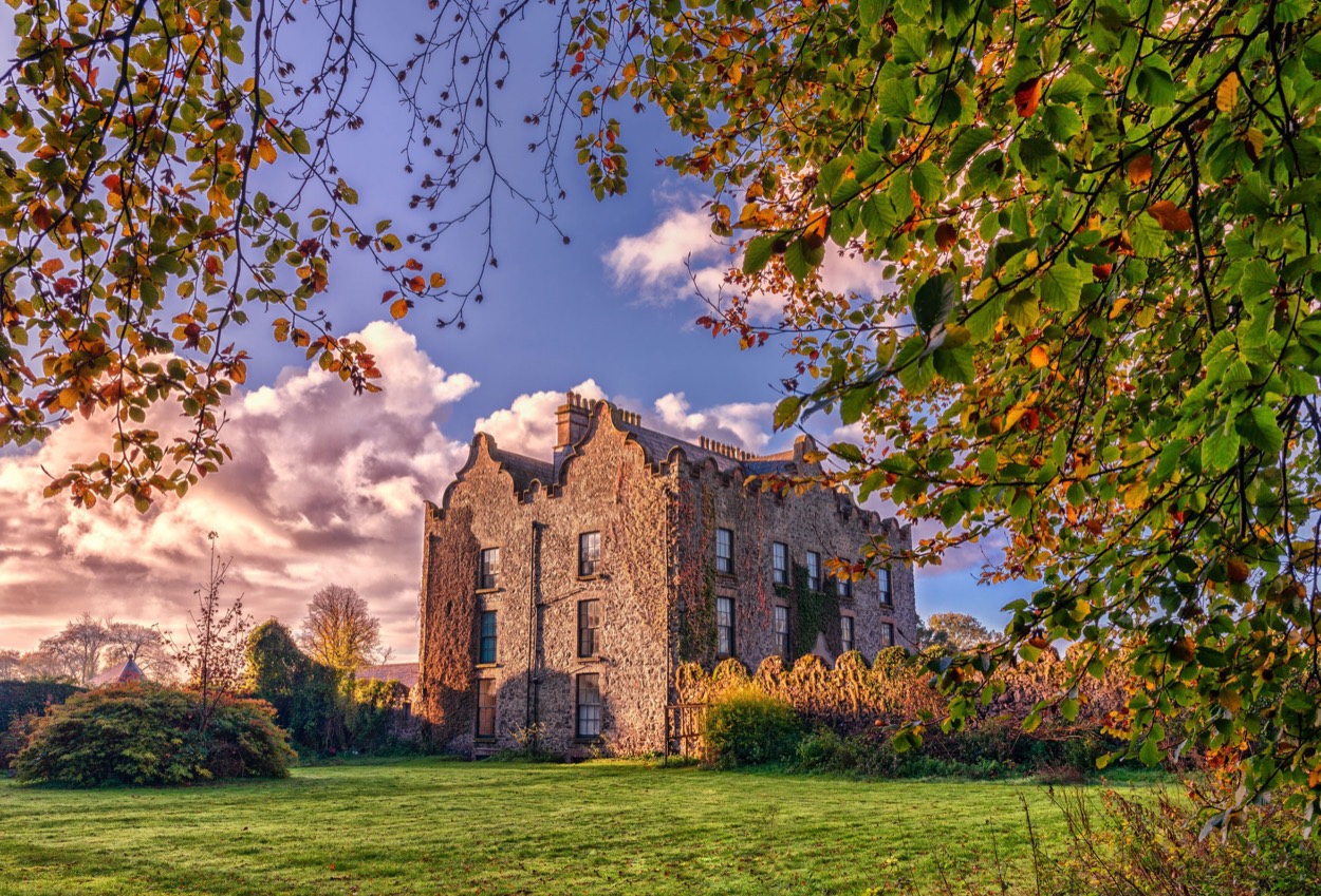 Galgorm Castle set in its lawns, framed by autumn trees at golden hour