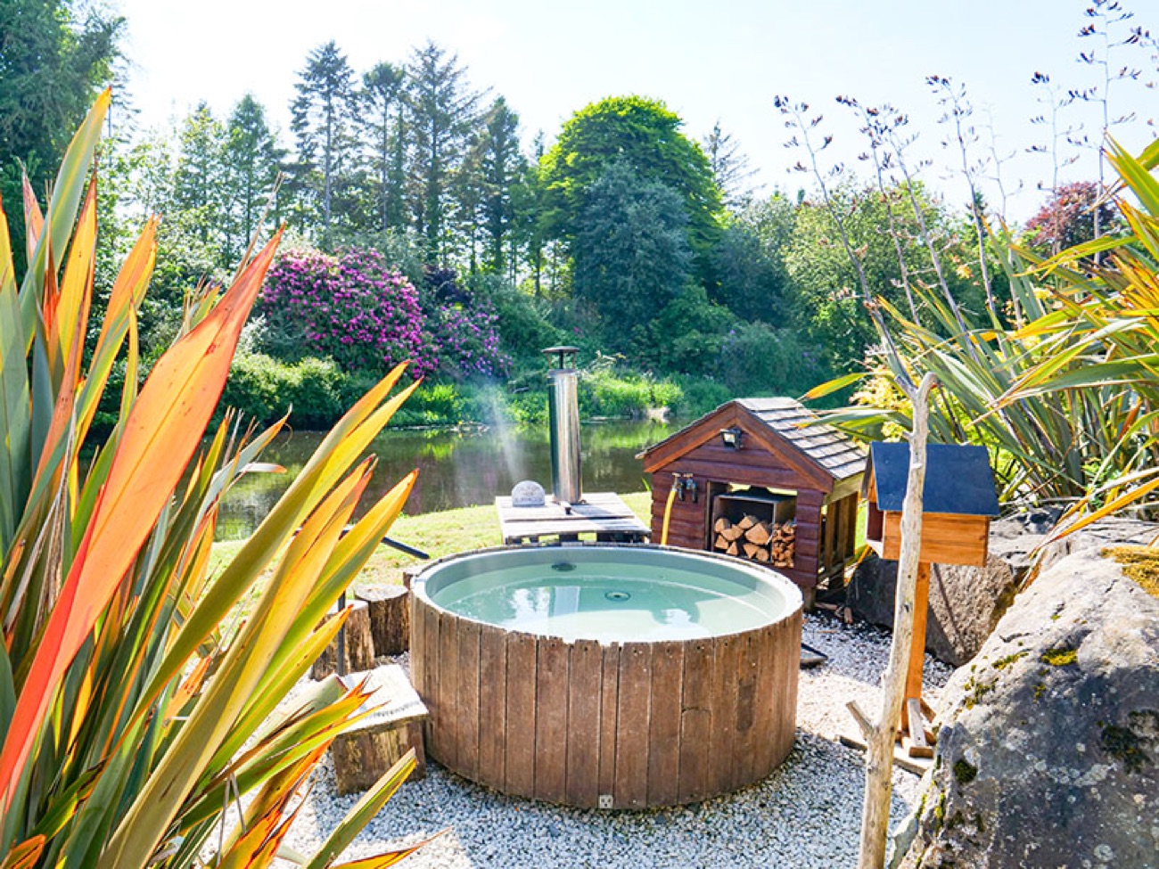 A wood-fired riverside bathing tub warming beside the River Maine at Galgorm, with a wood-burning heater and log store