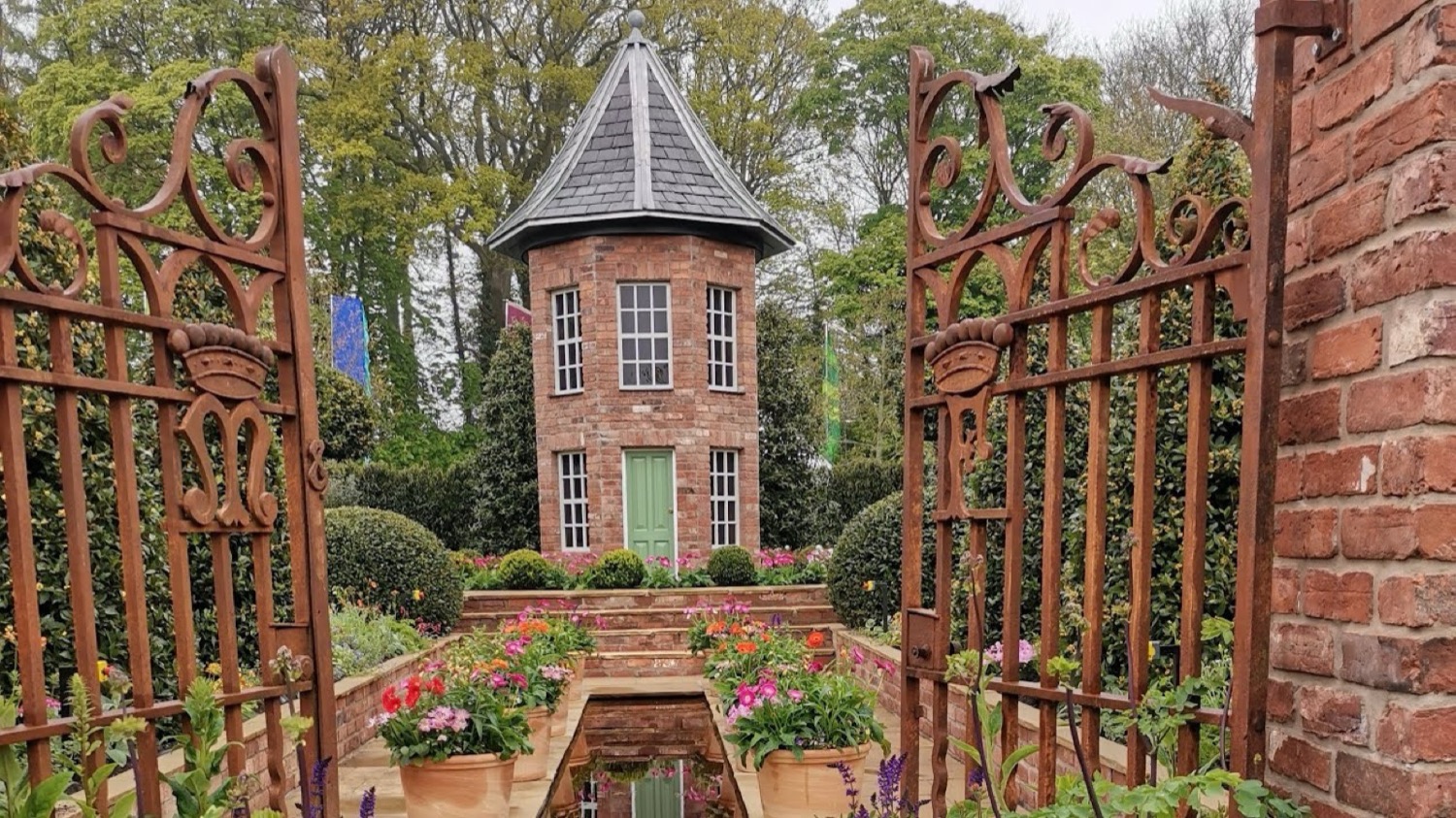 A show garden at Garden Show Ireland — a brick garden folly and water rill framed by ornate iron gates and tulips