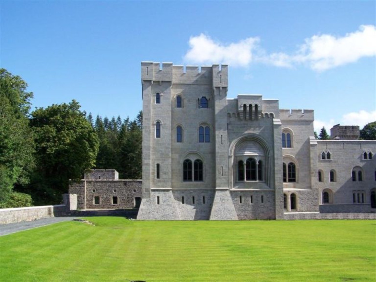 A battlemented stone tower and arched window of Gosford Castle under a blue sky above a striped green lawn
