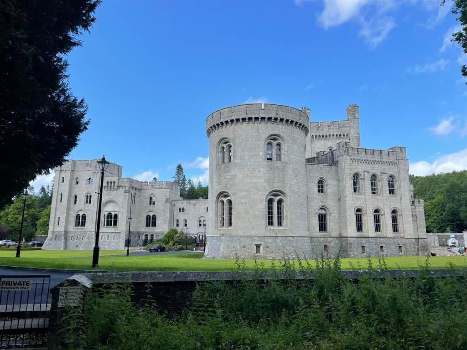 The vast grey Norman-revival Gosford Castle rising against a bright blue sky, its round tower and battlements above green lawns