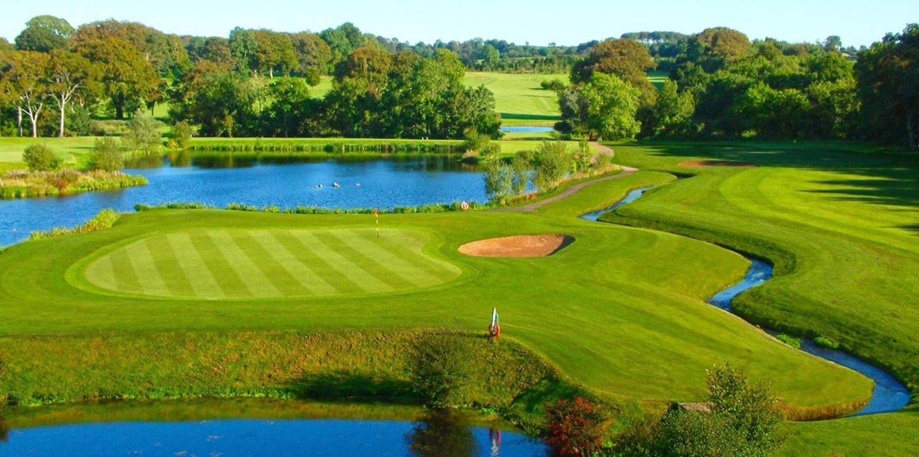 A manicured green and flag on Gracehill Golf Club, water and mature trees behind