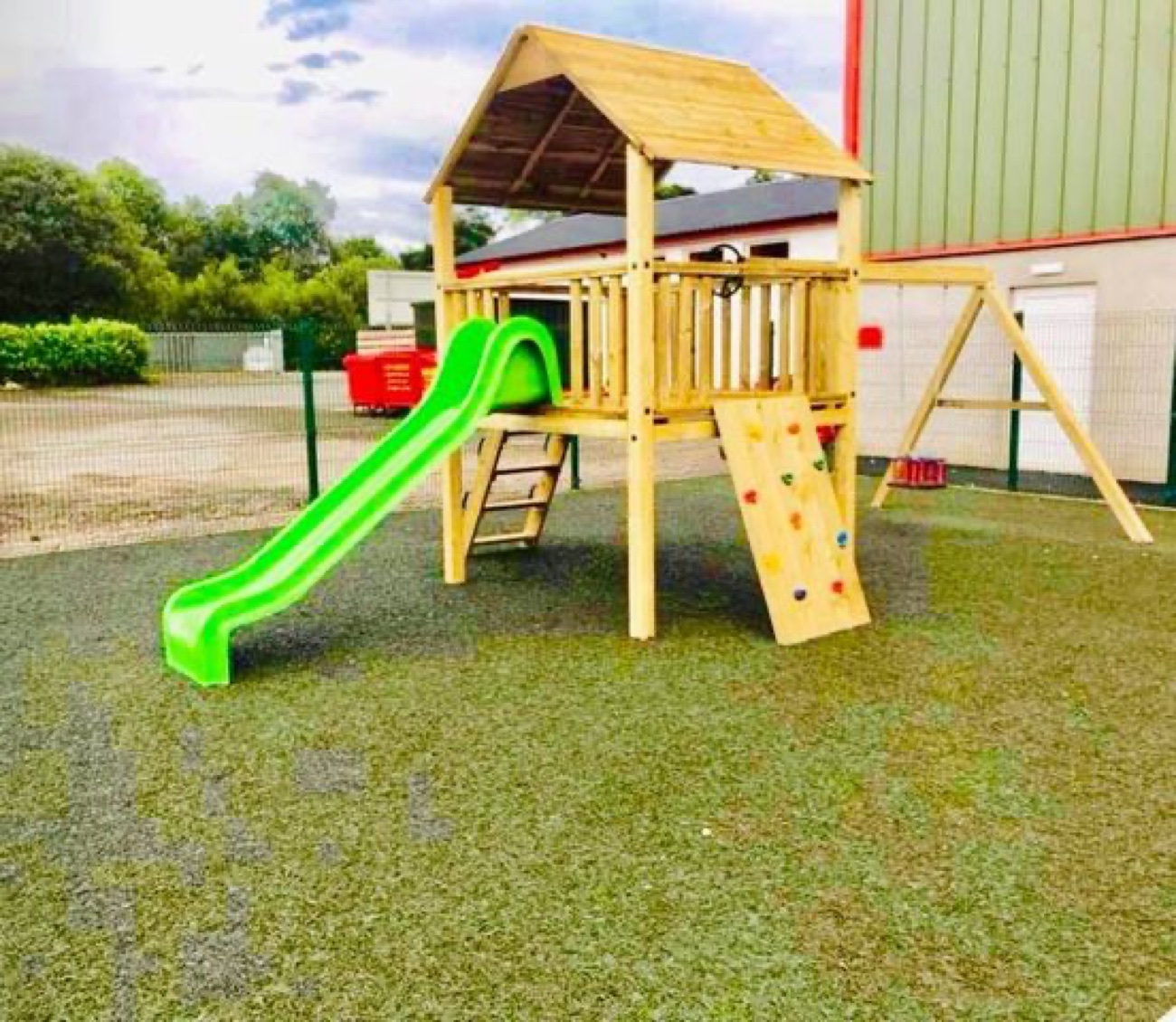 A wooden climbing frame with a green slide and a scramble wall in the Happy Dayz outdoor play area