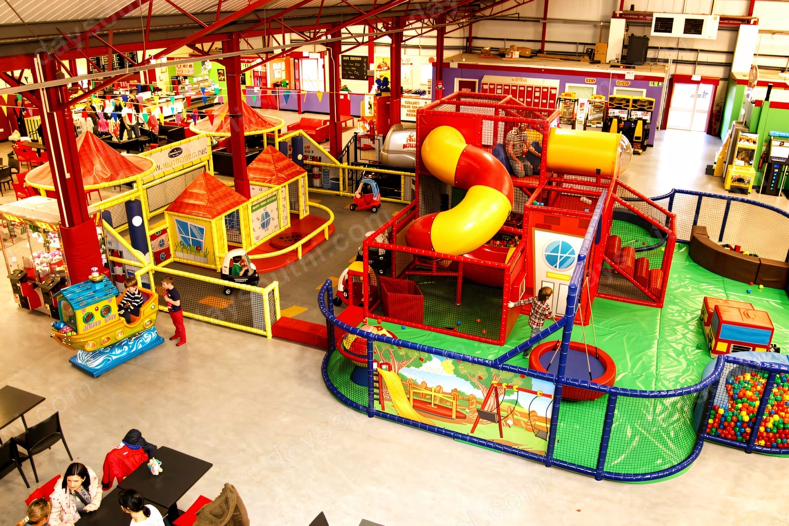 A big brightly-coloured indoor soft play at Happy Town Newtownards, with two multi-level themed frames, a yellow tube slide and café tables