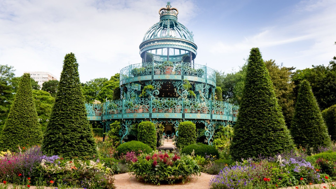 The turquoise ironwork Coronation Garden pavilion at Hazelbank Park with clipped topiary cones and blue sky