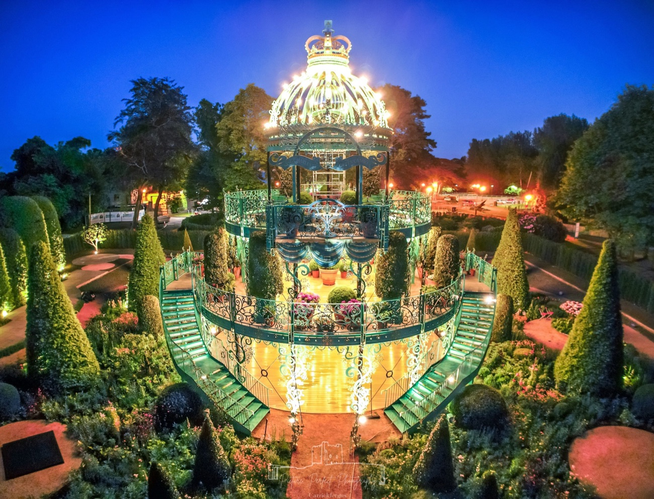 The Coronation Garden lit up at night, the ironwork pavilion glowing above the topiary