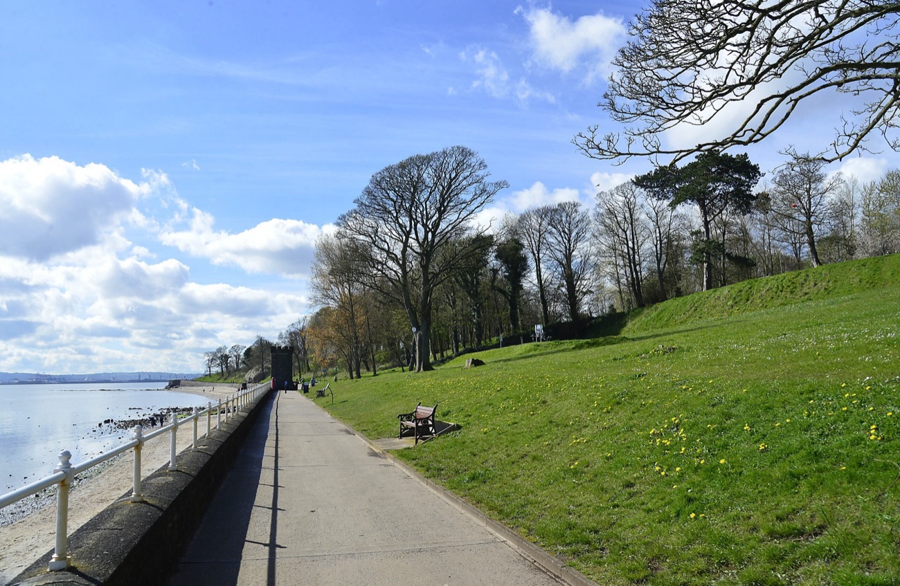 The sea wall promenade at Hazelbank with a grass bank, mature trees and big skies over the lough