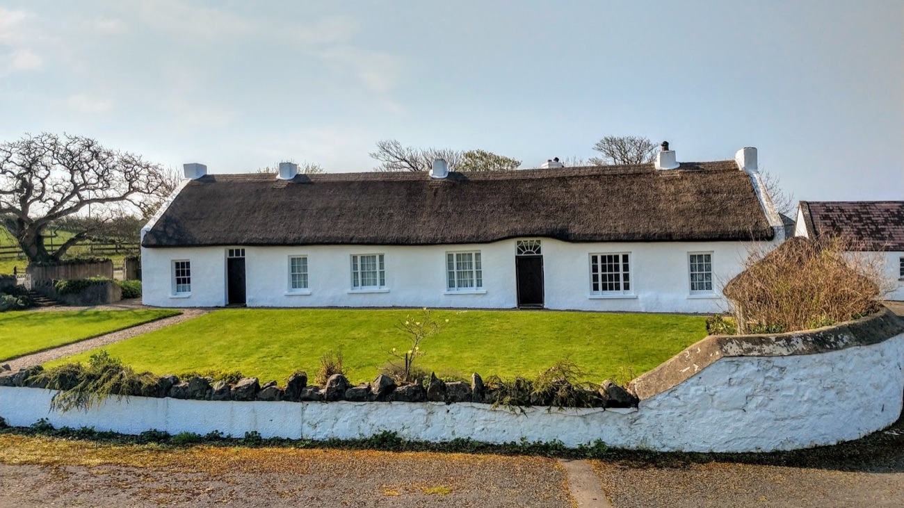 Hezlett House seen from the front on a sunny day, its dark thatched roof and white stub chimneys above a low whitewashed stone wall