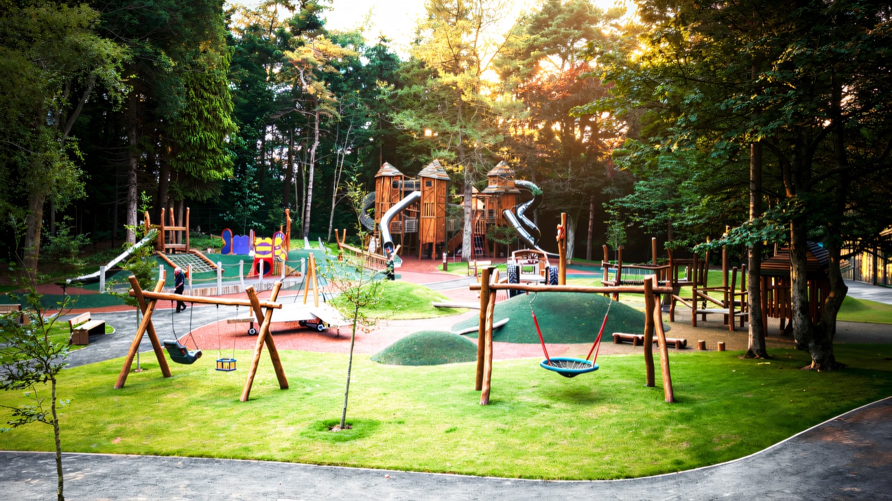 A wide view of the Hillsborough Forest play park with grass mounds, swings and play units among the trees